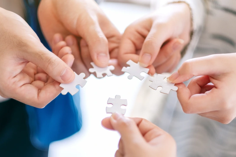 Zdjęcie 5 dłoni, które trzymają puzzle i chcą je złączyć.